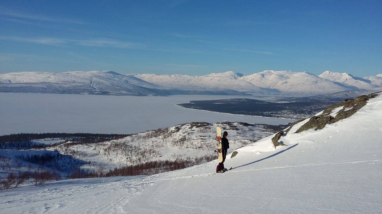 Skiløper på snødekt fjellrygg med utsikt over fjell og vann